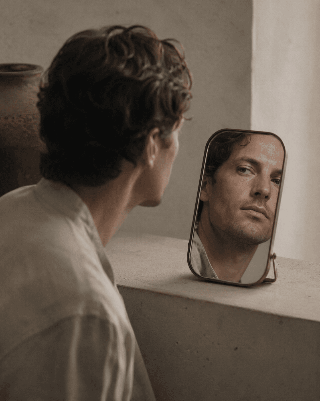 A man in profile watching his reflection in a mirror.